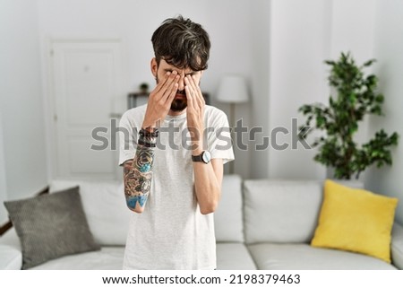 Hispanic man with beard at the living room at home rubbing eyes for fatigue and headache, sleepy and tired expression. vision problem 