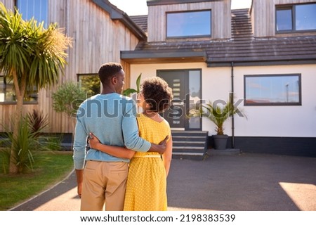 Rear View Of Couple Standing In Driveway In Front Of Dream Home Together Royalty-Free Stock Photo #2198383539