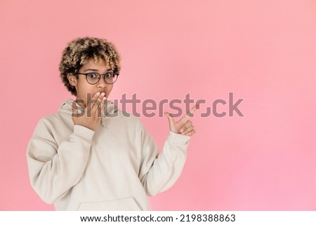 Astonished African American woman pointing copy space. Female model in hoodie and glasses showing blank space. Portrait, studio shot, presentation concept