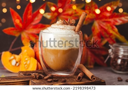 A glass of autumn pumpkin latte with whipped cream and spices. Coffee with pumpkin and cinnamon on a dark background, bokeh lights, vertical photo