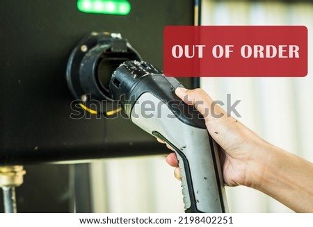 Out of order electric vehicle charging station. Electric vehicle charging station infrastructure problems. Hand holding EV charger that hasn't been used for a long time until the ants come to nest. Royalty-Free Stock Photo #2198402251