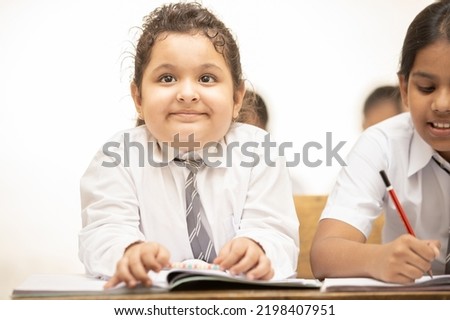 Portrait of happy indian schoolgirl sitting at desk in classroom, Elementary school, Education concept.