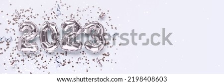 Banner with 2023 silver foil inflatable balloons, stars confetti and ribbons on a blue background. New Year's concept with copy space.