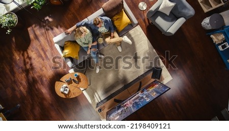 Top View Apartment: Lovely Couple Watching Television in the Stylish Living Room. Looking at the TV Display and Eating Popcorn. Girlfriend and Boyfriend Enjoy Sitcom on Streaming Service on Couch.