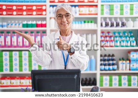 Middle age woman with tattoos working at pharmacy drugstore showing palm hand and doing ok gesture with thumbs up, smiling happy and cheerful 