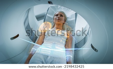 Female Patient Lying on a CT or PET or MRI Scan Bed, Moving Inside the Machine While it Scans Her Brain and Vital Parameters. AR Concept with Visual Effects In the Lab with High-Tech Equipment. Royalty-Free Stock Photo #2198432425
