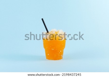 Refreshing Slushie drink. Orange Granizado in disposable plastic take away cup on blue background. Sweet citrus Shaved ice. Selective focus, copy space. Royalty-Free Stock Photo #2198437245