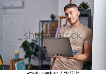 Young hispanic man artist smiling confident using laptop at art studio Royalty-Free Stock Photo #2198437449