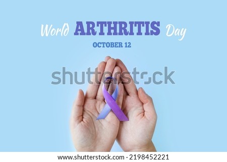 World Arthritis Day. Adult hands holding blue purple ribbon on blue background. RA rheumatoid arthritis illness disease Royalty-Free Stock Photo #2198452221
