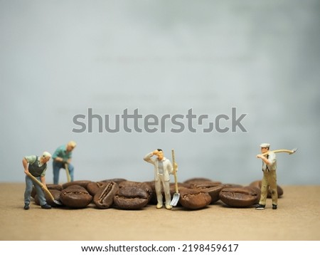 Miniature toy of worker and truck with coffee beans. Unfocus many stuff at table. Background is blurred. Toy photography concept.