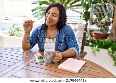 Hispanic brunette woman drinking a coffee and eating pastries at the terrace
