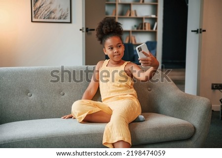 Making a selfie. Cute black girl in casual clothes is at home at daytime.