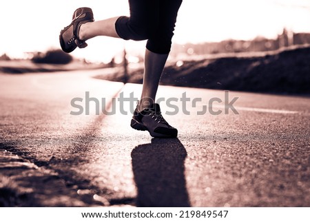 Young lady running on a road during sunset. Selective focus. Low depth of field. Detail of sport feet on trail. Black and white photography. Sepia. Cream tone.
