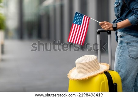 Unrecognizable woman with straw hat on yellow suitcase holding flag of the US, posing in airport, panorama with copy space. Travelling, tourism, vacation, holidays, education abroad concept Royalty-Free Stock Photo #2198496419
