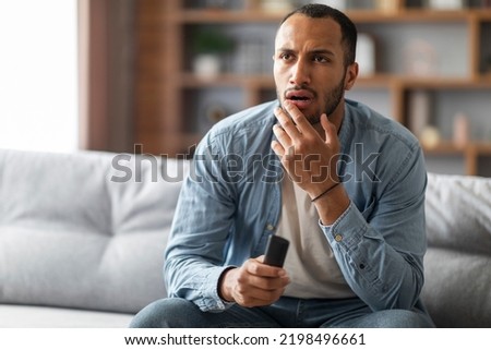 Shocked Black Man With Remote Controller In Hand Sitting On Couch At Home, Confused Young African American Guy Watching Tv Show In Living Room, Emotionally Reacting To Shocking Content, Copy Space Royalty-Free Stock Photo #2198496661