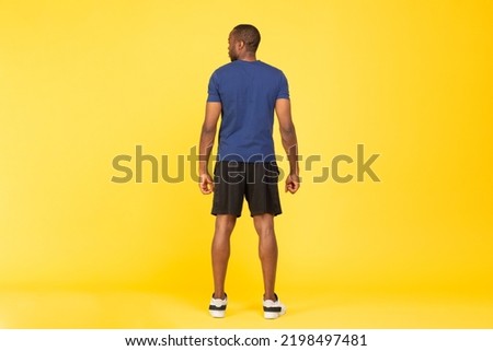Rear View Of Unrecognizable Sporty Black Man Posing Standing Back To Camera Wearing Fitwear Over Yellow Studio Background. Fitness Workout Concept. Full Length Shot Royalty-Free Stock Photo #2198497481
