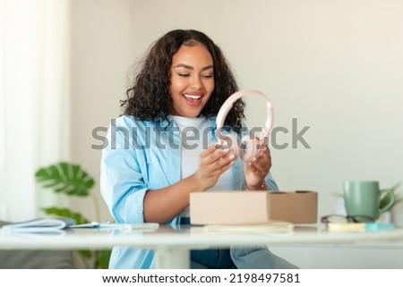 Gadgets Shopping. Excited African American Woman Unpacking Cardboard Box With Headphones Sitting At Desk At Home. Successful Delivery Concept. Selective Focus