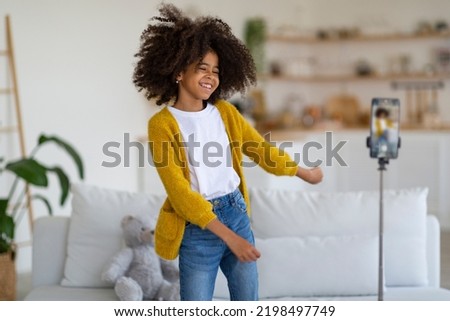 Emotional talented african american school girl broadcasting from home, happy black kid dancing and laughing, looking at smartphone camera, famous kids blogger recording video for followers