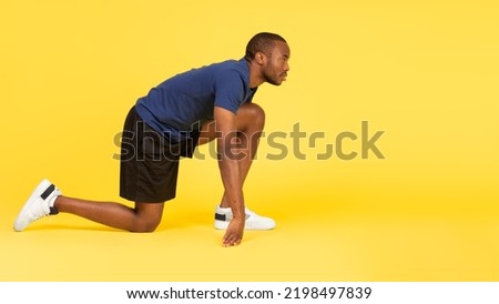 Side View Of African American Runner Guy Standing In Crouch Start Position Looking Aside Over Yellow Background. Male Athlete Posing Ready For Marathon Race In Studio. Sport Of Athletics