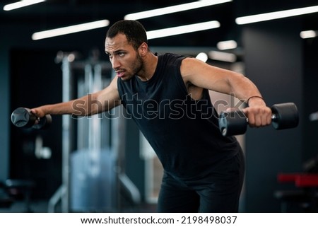 Muscular Young Man Doing Dumbbell Lateral Raise Exercise At Gym, Motivated African American Male Athlete Training Muscles At Modern Fitness Club, Enjoying Bodybuilding Workout, Free Space Royalty-Free Stock Photo #2198498037