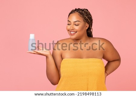 Skincare Cosmetics. Oversized African American Female Holding Micellar Water Bottle Advertising Cosmetic Product Standing Posing Wrapped In Towel Over Pink Background. Studio Shot Royalty-Free Stock Photo #2198498113