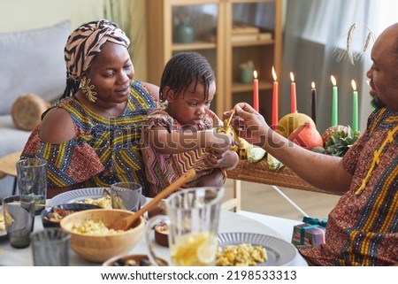 African little girl opening present together with her parents giving her for Kwanzaa holiday