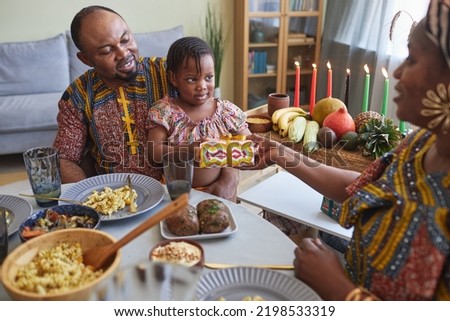 African parents giving present to their little daughter for holiday while they sitting at dining table