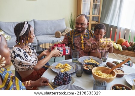 African family giving presents to each other during holiday dinner at table at home, they celebrating Kwanzaa