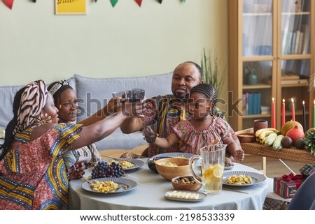 African family in national costumes toasting with drinks sitting at dining table, they celebrating traditional holiday