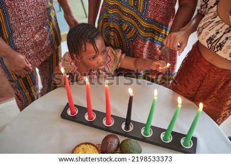Above view of African little girl lighting candles at table together with her family in national costumes to celebrate holiday