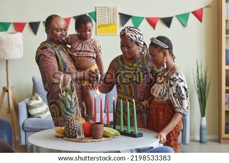 African family of four celebrating Kwanzaa at home, they lighting seven candles together on table