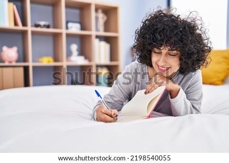 Young middle east woman writing on notebook lying on bed at bedroom