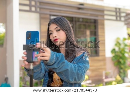 A female teenager with a serious expression fixes her phone on a tripod as she sets up for recording a dance video. Royalty-Free Stock Photo #2198544373