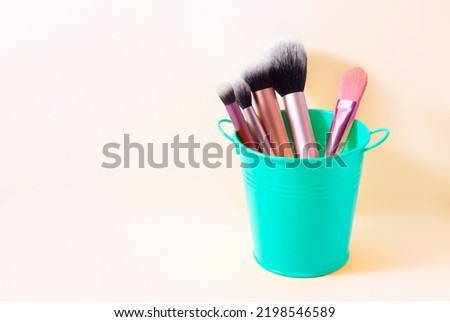 green pot with pink makeup brushes on yellow background