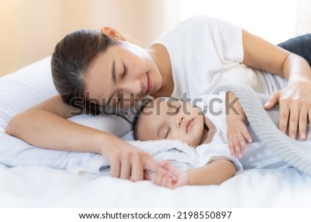 Mom and Newborn,Happy family concept.Close up view of beautiful Asian mother and her sleeping newborn baby.Mother holding baby hand in one hand and holding hand the baby with eyes closing and smiling.