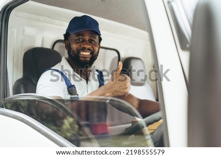 Portrait of courier black man in the truck thumb up and smiling to camera while sitting in driver seat, Optimistic man worker with delivery occupation. Royalty-Free Stock Photo #2198555579