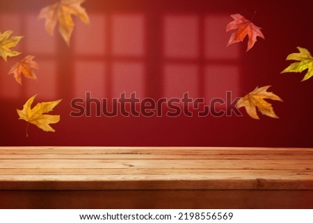 Empty wooden  table over trendy red wall background with window shadow and fall leaves.  Autumn season mock up for design and product display.