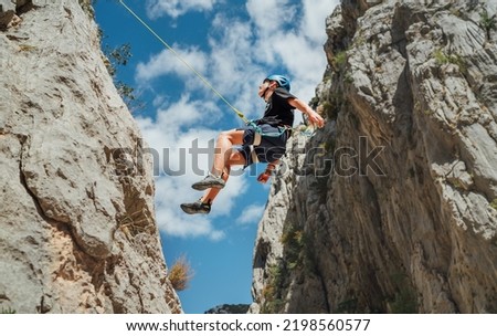 Climber teenager boy in protective helmet abseiling from vertical cliff rock wall using rope Belay device, climbing harness in Paklenica canyon in Croatia. Active extreme sports time spending concept Royalty-Free Stock Photo #2198560577
