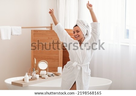 Joyful Woman Singing And Dancing Having Fun In Modern Bathroom Indoor. Lady Enjoying Selfcare Beauty Routine Posing Wearing Bathrobe At Home. Spa And Bodycare Cosmetics Concept