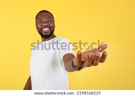 Look At This. Happy  Man Showing Invisible Object Holding It On Hand Smiling To Camera Advertising Product Standing Over Yellow Background. Studio Shot