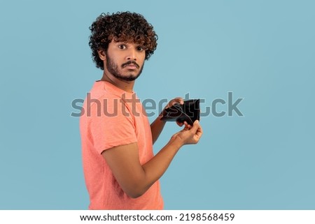 Financial crisis and bankruptcy while COVID-19 pandemic concept. Sad eastern man showing empty wallet at camera, short of money, spent money, blue studio background, copy space Royalty-Free Stock Photo #2198568459