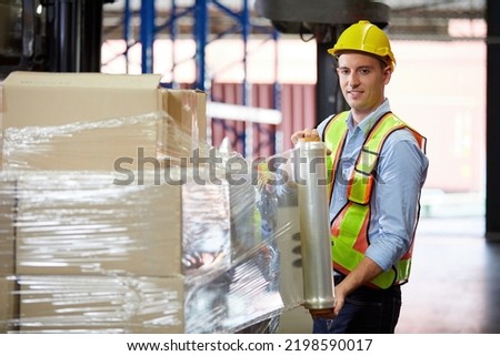 factory worker or warehouser wrapping stretch film parcel on pallet covered cardboard boxed in warehouse storage
