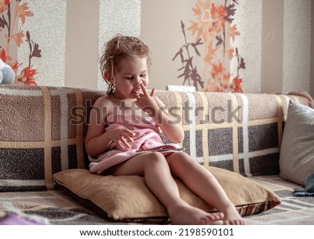 A teenage girl sits on a sofa and picks her finger in her nostril. The child, after taking a shower, wrapped in a towel, sat down on Ivan to watch a cartoon on a smartphone and picks his nose
