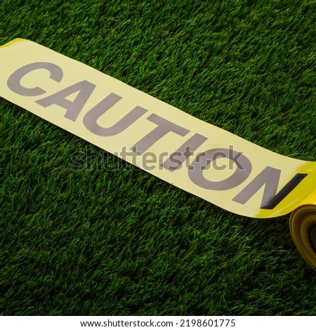 Yellow ribbon with the inscription - caution on green grass. Warning sign about danger, destroyed buildings, facilities under construction, bad road, quarantine.