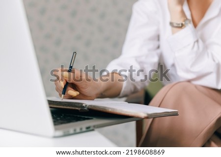 Closeup woman psychotherapist is holding notebook and making notes during online therapy session, background internet laptop with web call.