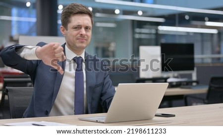 Businessman Showing Thumbs Down Sign While using Laptop in Office