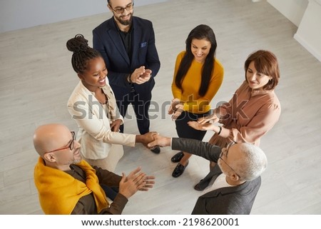 Top view of smiling diverse business partners handshake greet get acquainted at office team meeting. Senior businessman shake hand congratulate ethnic female colleague with promotion or success. Royalty-Free Stock Photo #2198620001