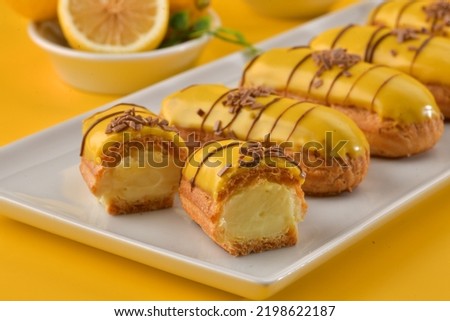 Glazed eclairs with cream filling on a white plate on yellow background. Lemon on the eclair. Eclairs made with cream and lemon. Delicious eclairs at concepts of dessert.  Royalty-Free Stock Photo #2198622187