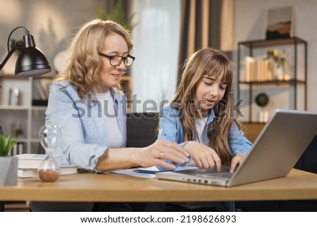 Mother teach young daughter to do homework, using digital laptop at home. E-learning lifestyle, happy family homeschooling, children remote distance education, or internet technology concept