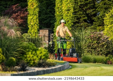 Large and Beautiful Landscape Garden in the Backyard of Residential House. Professional Landscaper in Protective Headphones Taking Care of Design Appearance by Mowing the Lawn. Royalty-Free Stock Photo #2198643433